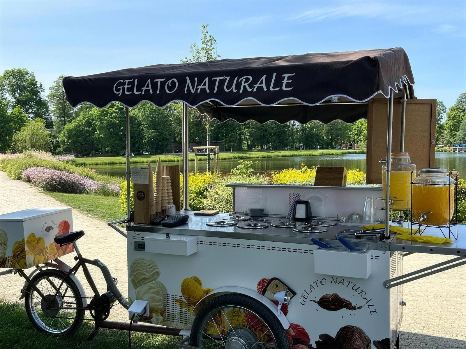Rower Gelato Naturale nad stawem w parku, rabaty kwiatów i stojaki z waflami