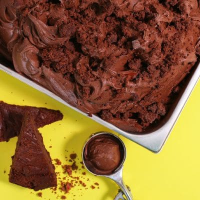 Lody brownie z kawałkami ciasta w kuwecie, obok ciasto i gałkownica na żółtym tle