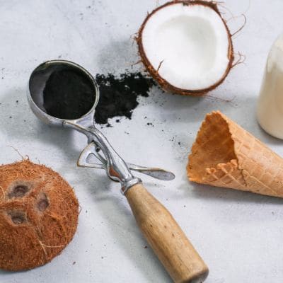 Czarne lody kokosowe w gałkownicy, obok połówka kokosa i rożek