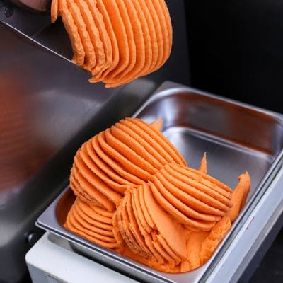 Pomarańczowe lody wychodzą z maszyny do stalowej kuwety