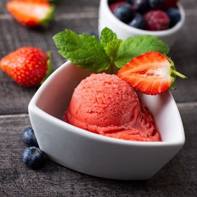 Gałka sorbetu truskawkowego w białej miseczce, obok truskawki i borówki