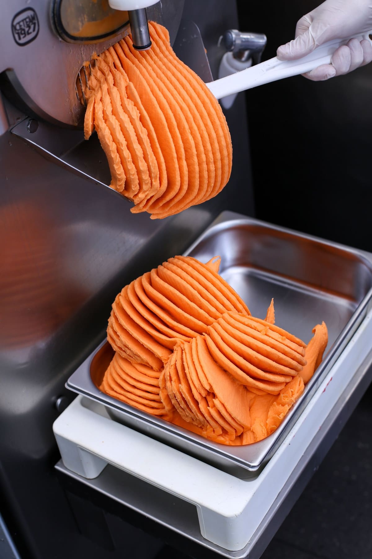 Pomarańczowe lody wychodzą z maszyny do stalowej kuwety
